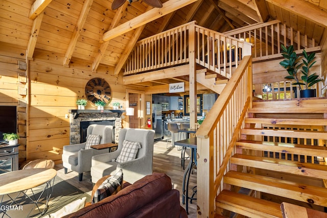 stairs featuring beamed ceiling, a stone fireplace, wood walls, and wood ceiling