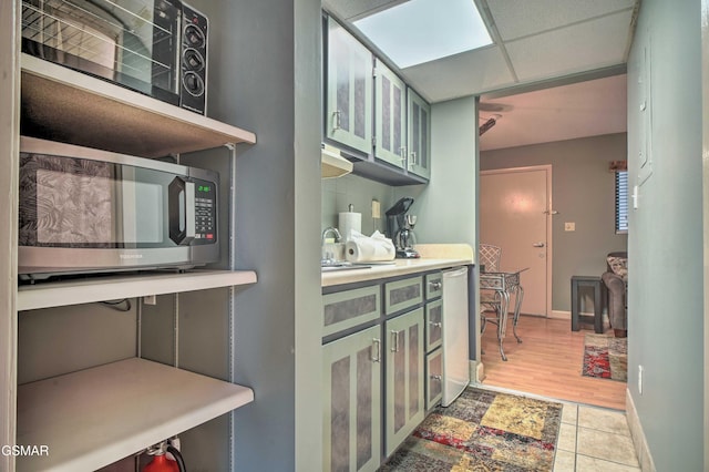 kitchen with light countertops, stainless steel microwave, baseboards, light tile patterned flooring, and green cabinetry