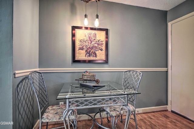 dining space featuring a textured ceiling, baseboards, and wood finished floors