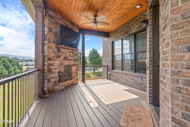 wooden terrace with ceiling fan and an outdoor stone fireplace