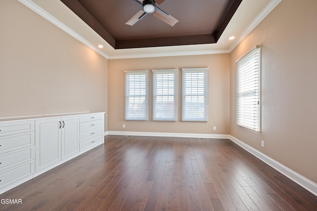 empty room with dark hardwood / wood-style flooring, a tray ceiling, and ceiling fan