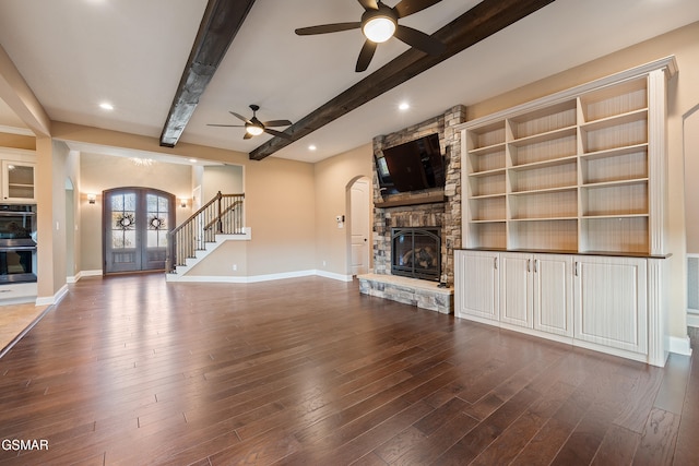 unfurnished living room with beam ceiling, a stone fireplace, ceiling fan, and wood-type flooring