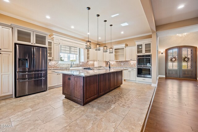 kitchen featuring french doors, an island with sink, appliances with stainless steel finishes, decorative light fixtures, and light stone counters