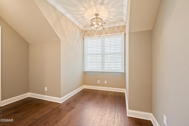 empty room featuring dark hardwood / wood-style floors, lofted ceiling, ornamental molding, and a chandelier