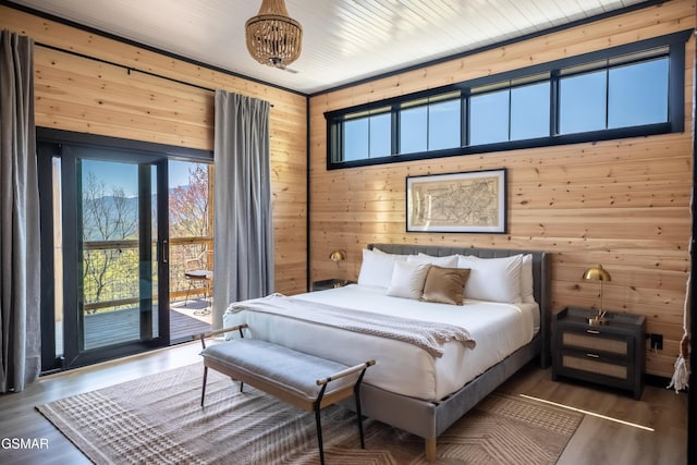 bedroom with wood finished floors, multiple windows, wood walls, and access to outside