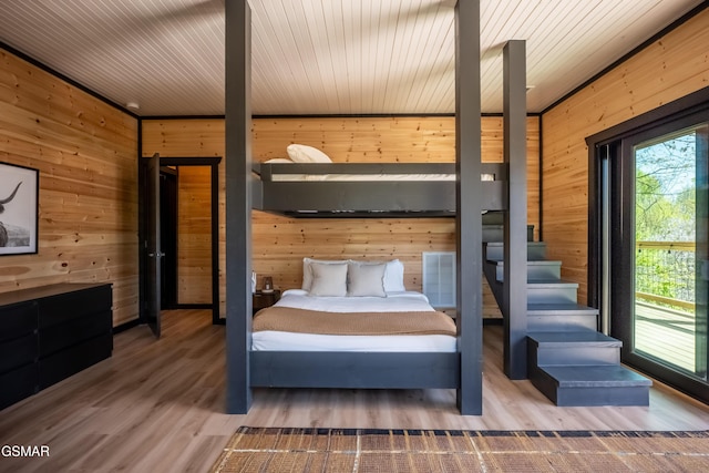 bedroom with wooden walls, multiple windows, and wood finished floors