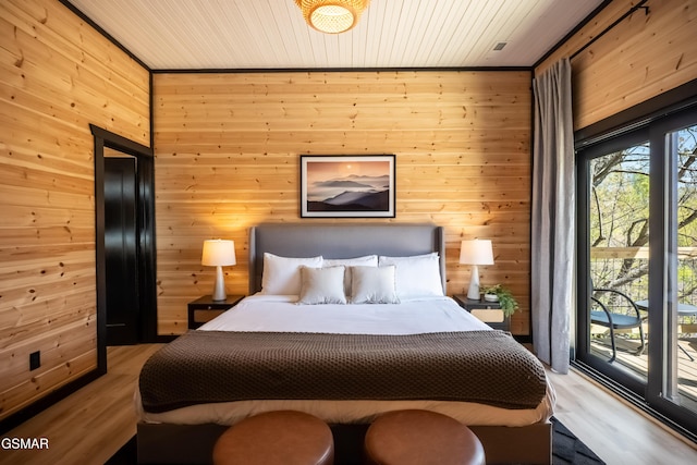 bedroom featuring light wood-style floors, access to exterior, and wood walls