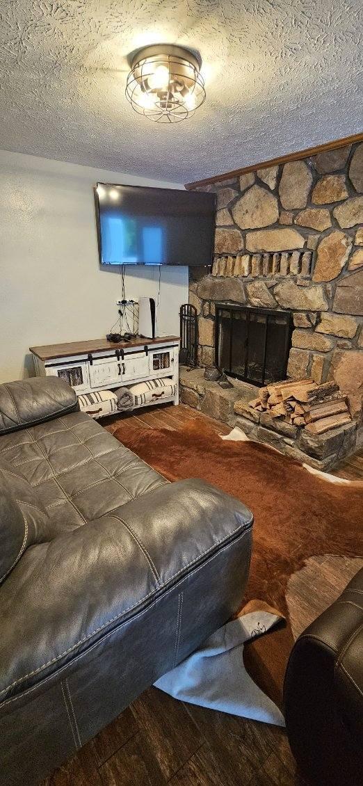 living room with a textured ceiling, hardwood / wood-style flooring, and a stone fireplace