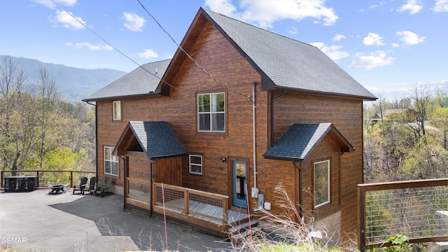 rear view of house featuring a patio area, a mountain view, roof with shingles, and an outdoor fire pit