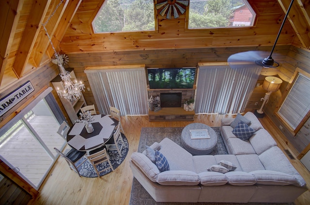 living room with wooden walls, a fireplace, high vaulted ceiling, and a chandelier