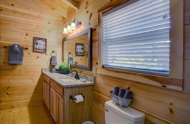 bathroom featuring vaulted ceiling with beams, vanity, toilet, and wood walls