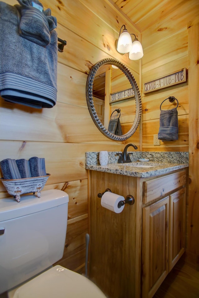 bathroom featuring vanity, toilet, and wooden walls