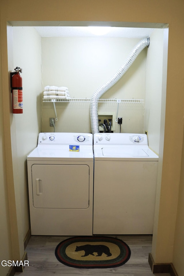 washroom with washing machine and clothes dryer, wood finished floors, and laundry area