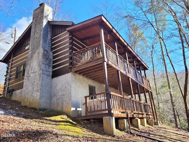 view of property exterior featuring log siding, a deck, and a chimney