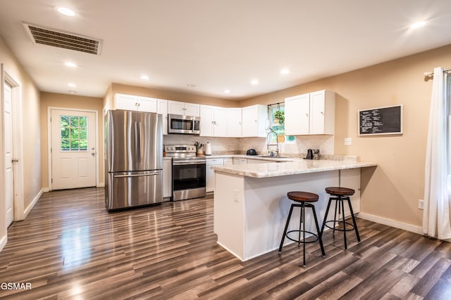 kitchen featuring appliances with stainless steel finishes, a peninsula, a sink, dark wood finished floors, and white cabinets
