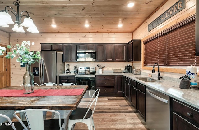 kitchen featuring sink, light stone counters, wood walls, appliances with stainless steel finishes, and light wood-type flooring