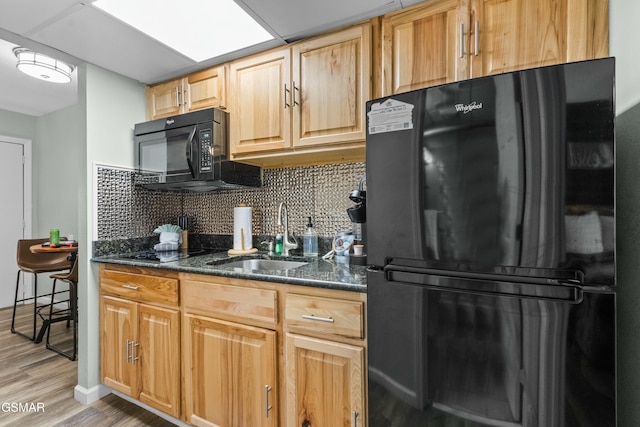 kitchen with dark stone counters, black appliances, sink, tasteful backsplash, and light hardwood / wood-style floors