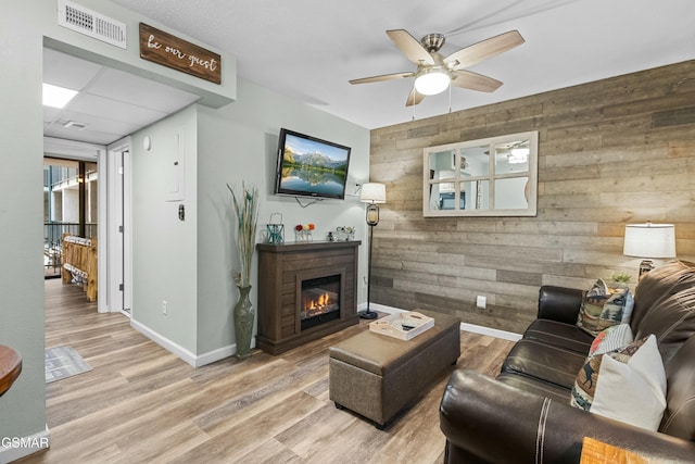 living room featuring wood walls, ceiling fan, and light wood-type flooring