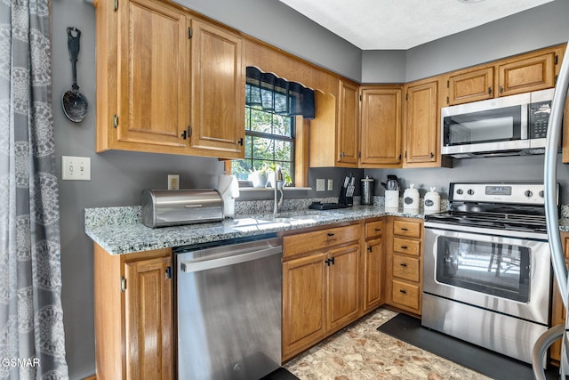 kitchen featuring brown cabinetry, a sink, appliances with stainless steel finishes, and light stone countertops