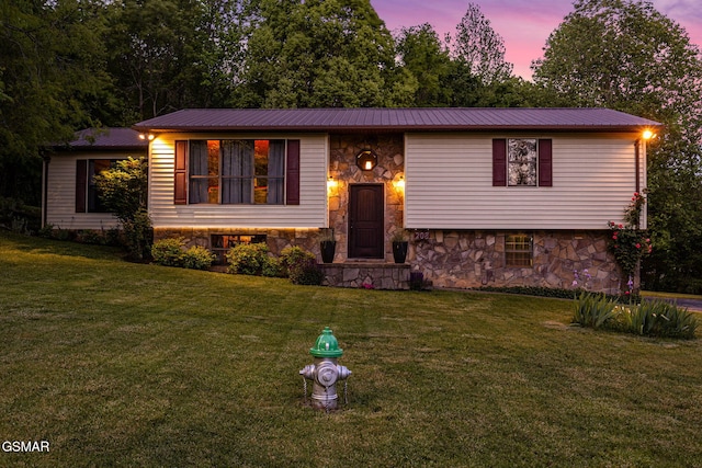 raised ranch featuring a front yard, metal roof, and stone siding