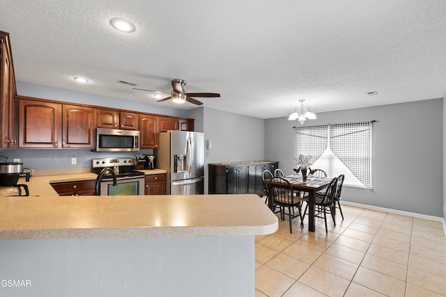 kitchen featuring a peninsula, ceiling fan with notable chandelier, light countertops, a textured ceiling, and appliances with stainless steel finishes