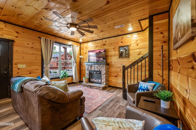 living room with wood walls, wooden ceiling, ceiling fan, a fireplace, and wood-type flooring