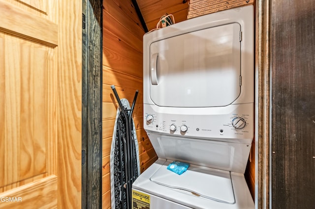 clothes washing area featuring wood walls and stacked washing maching and dryer