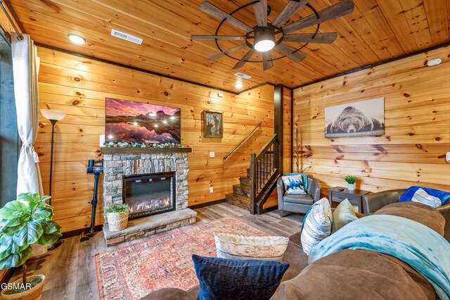 living room with hardwood / wood-style floors, ceiling fan, a stone fireplace, and wood ceiling