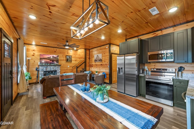 dining room featuring hardwood / wood-style flooring, a stone fireplace, ceiling fan, and wood ceiling