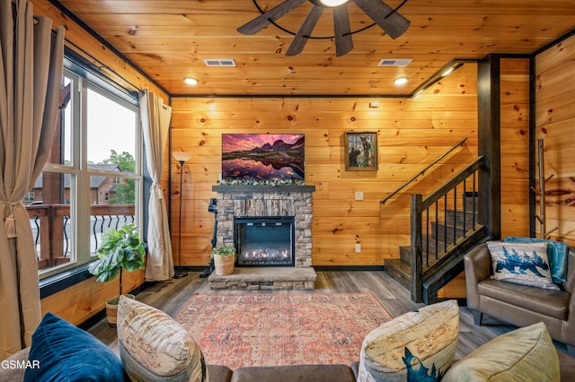 living room with dark wood-type flooring, a stone fireplace, wooden walls, ceiling fan, and wood ceiling