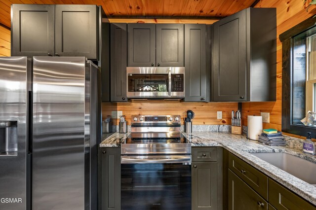 kitchen with wood walls, light stone counters, and appliances with stainless steel finishes