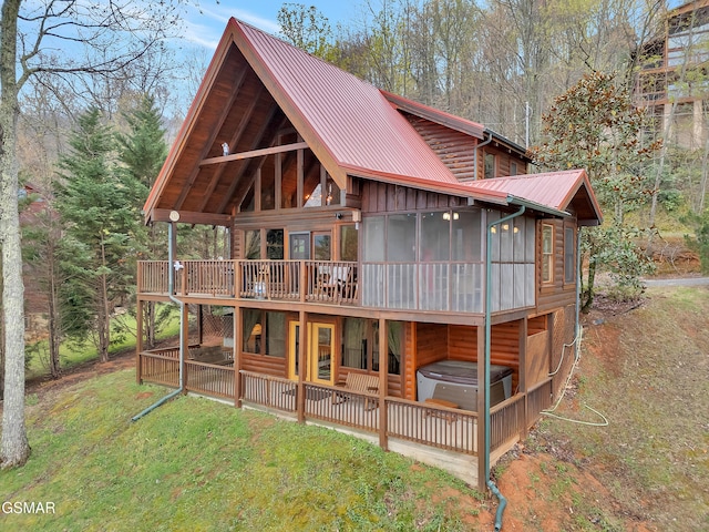 rear view of house featuring metal roof, a wooden deck, a lawn, a sunroom, and a jacuzzi