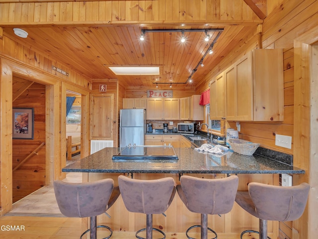 kitchen featuring stainless steel appliances, a peninsula, visible vents, wood walls, and track lighting