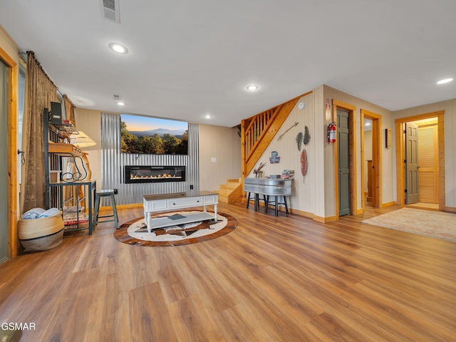 living area featuring a glass covered fireplace, visible vents, recessed lighting, wood finished floors, and stairs