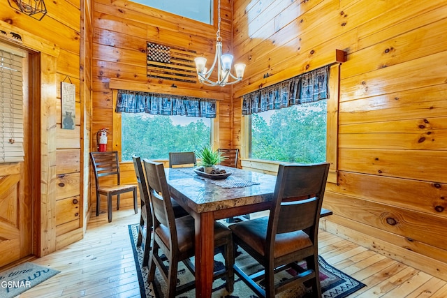 dining area featuring wood walls, light hardwood / wood-style flooring, and an inviting chandelier