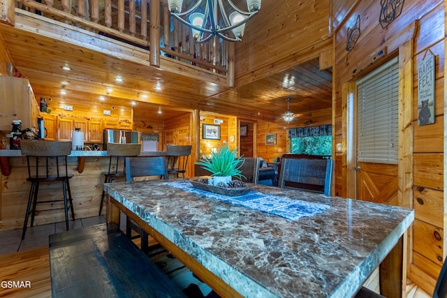 dining area with wood walls, ceiling fan with notable chandelier, wooden ceiling, and dark hardwood / wood-style floors