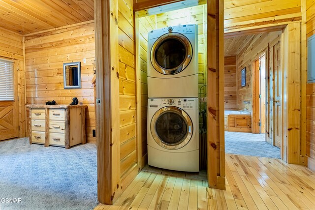 clothes washing area with light hardwood / wood-style floors, wooden ceiling, stacked washer and dryer, and wooden walls