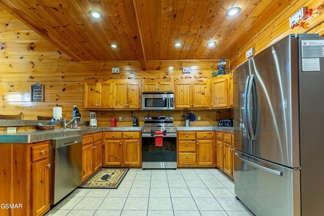 kitchen with light tile patterned floors, stainless steel appliances, wooden walls, and sink