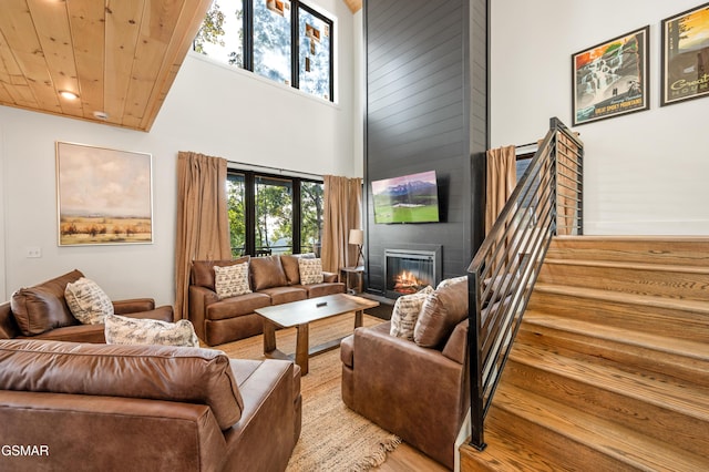 living room with a fireplace, a towering ceiling, wood finished floors, stairs, and recessed lighting