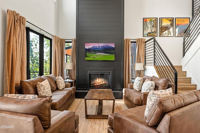 living area with wood finished floors, a large fireplace, a high ceiling, and stairs