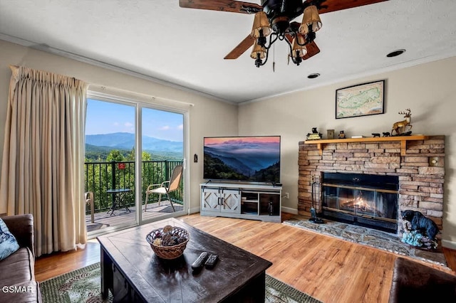 living area with crown molding, ceiling fan, baseboards, a fireplace, and wood finished floors