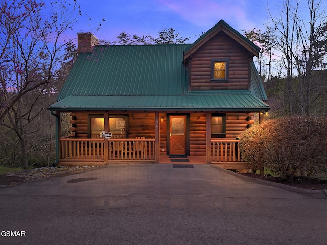 cabin with a porch, a chimney, metal roof, and log siding