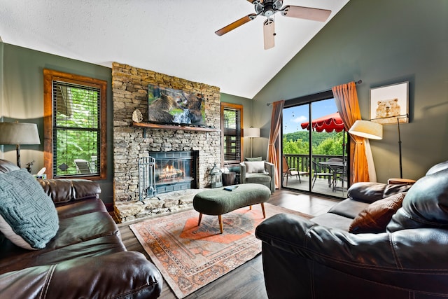 living room with light wood-type flooring, a textured ceiling, ceiling fan, high vaulted ceiling, and a stone fireplace