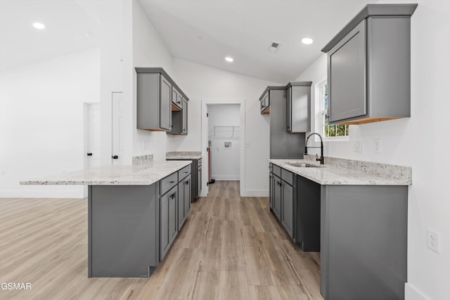 kitchen with lofted ceiling, sink, light hardwood / wood-style flooring, gray cabinets, and light stone counters