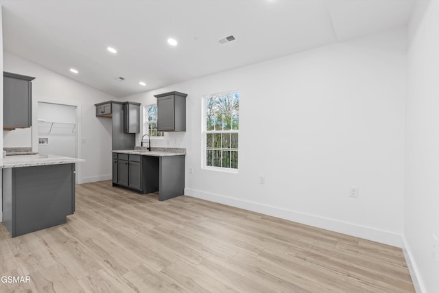 kitchen featuring light stone counters, vaulted ceiling, sink, light hardwood / wood-style flooring, and gray cabinets