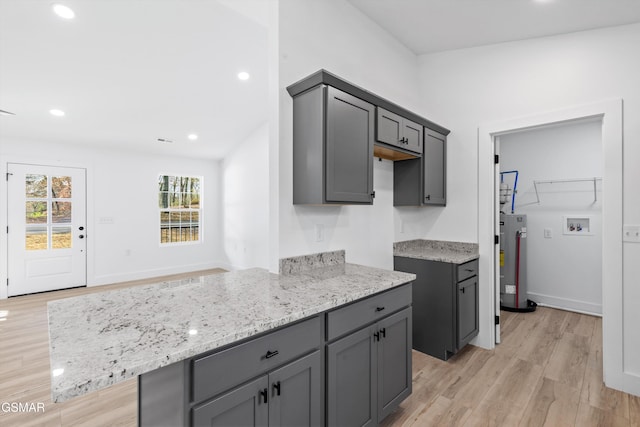 kitchen featuring gray cabinets, water heater, light hardwood / wood-style floors, and light stone counters