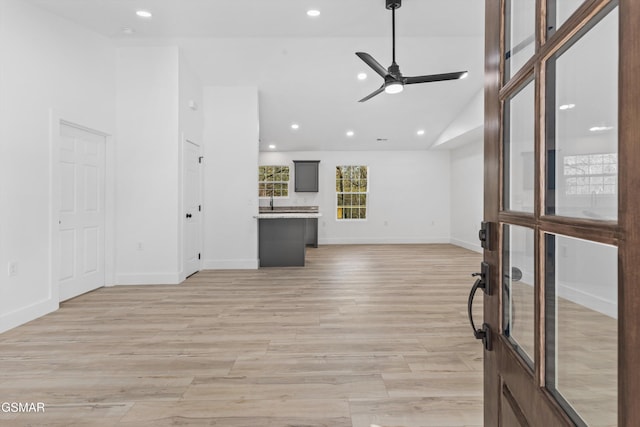 unfurnished living room with ceiling fan, vaulted ceiling, and light wood-type flooring