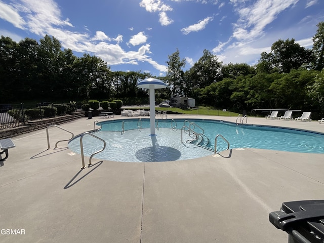 community pool featuring fence, a patio area, and view of wooded area