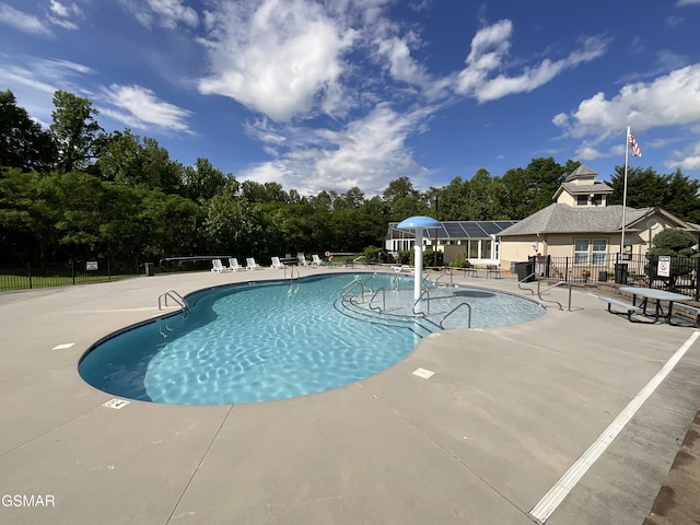 community pool featuring fence, a patio, and view of scattered trees