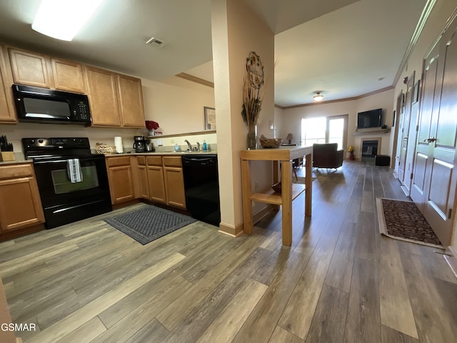 kitchen featuring black appliances, light wood-style flooring, ornamental molding, open floor plan, and light countertops
